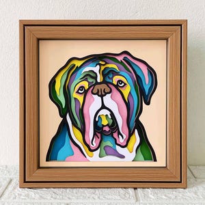 May include: A colorful paper art piece of a dog's face in a wooden frame. The dog's face is made up of different colored paper layers, creating a 3D effect. The frame is a light brown wood with a simple design.