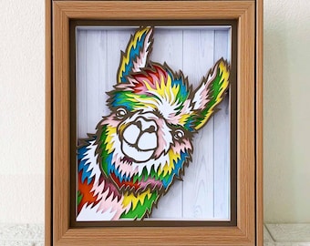 May include: A colorful, layered paper cutout of a llama's head peeking out of a wooden frame. The llama is smiling and has a rainbow-colored coat.