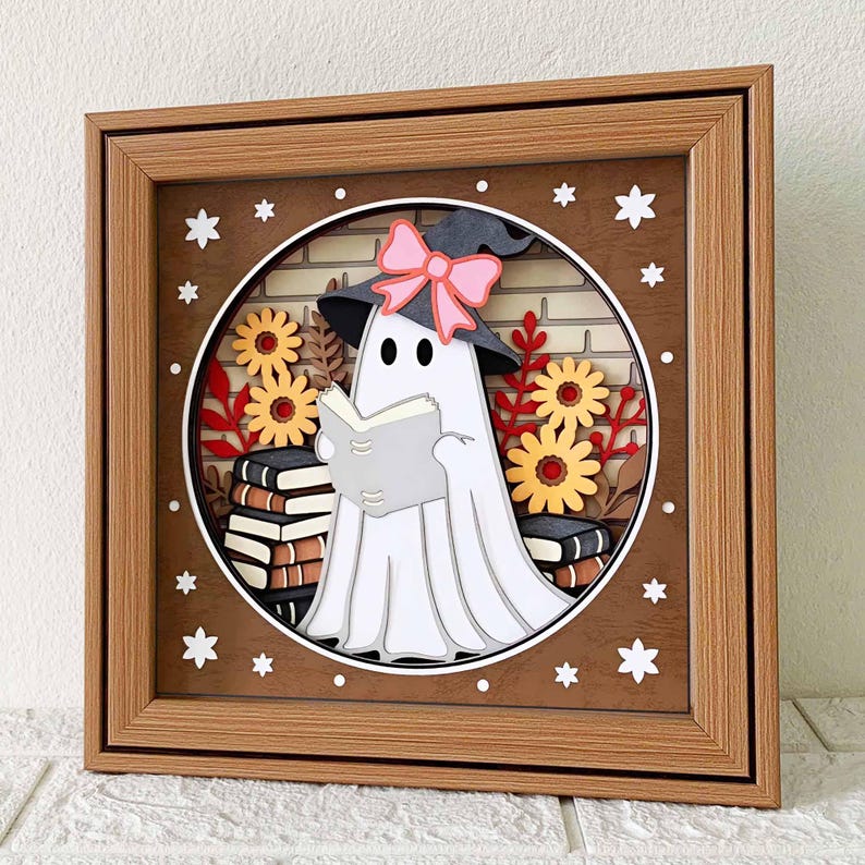 Op de afbeelding: Een witte geest met een roze strik en een heksenhoed leest een boek in een bruin houten frame met een bakstenen achtergrond en herfstbladeren.