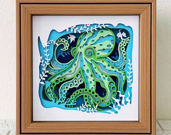 Puede incluir: Una obra de arte en papel enmarcada que representa un pulpo con tentáculos verdes y azules rodeado de algas y peces. El pulpo está en un estilo 3D, con los tentáculos superpuestos y recortados.