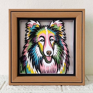 May include: A colorful paper cut-out of a dog's head in a wooden frame. The dog has a pink, yellow, blue, and green layered design.