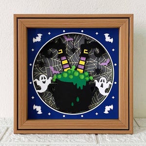 May include: A framed Halloween-themed artwork featuring a black cauldron with green bubbling liquid, witch legs, spiders, bats, and ghosts. The artwork is set against a blue background with a white web design and a brown wooden frame.