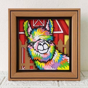 May include: A colorful papercraft llama peeking out from behind a red barn with a white picket fence. The llama has a rainbow-colored coat and a white face.
