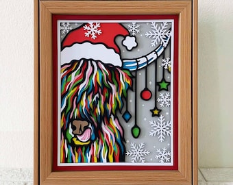 May include: A framed paper art piece of a colorful Highland Cow wearing a Santa hat with a string of Christmas ornaments hanging from the hat. The background is a light gray with snowflakes.