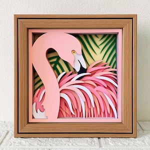 May include: A pink flamingo papercraft sculpture with layered feathers and a green tropical leaf background. The flamingo is positioned to look like it is peeking out from behind the leaves.