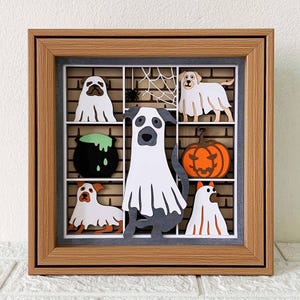 May include: A framed shadow box with a Halloween theme featuring six ghost dogs and a pumpkin. The dogs are all wearing ghost costumes and are in different poses. The pumpkin is carved with a spooky face.