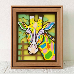 May include: A colorful paper cut-out of a giraffe's head in a wooden frame. The giraffe has yellow, green, blue, pink, and orange spots. The background is yellow with green leaves.