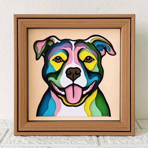 May include: A colourful, layered paper art piece depicting a pit bull terrier with a pink tongue sticking out. The dog's fur is a mix of blue, green, yellow, and purple.