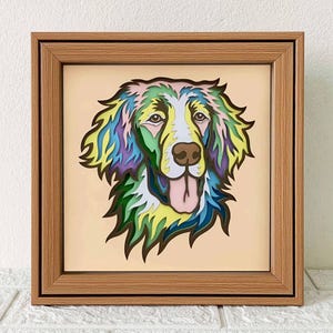 May include: A framed paper art piece of a dog's head. The dog is a multi-colored, layered paper design with a light pink background.