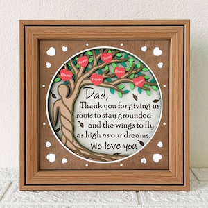 Könnte beinhalten: Ein gerahmtes Wandbild aus Holz mit braunem Hintergrund und einem grünen Baum mit roten Herzen. Der Baum ist von weißen Herzen umgeben und dem Text "Papa, Danke, dass du uns Wurzeln gegeben hast, um geerdet zu bleiben, und Flügel, um so hoch zu fliegen wie unsere Träume. Wir lieben dich".