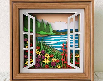 Puede incluir: Una escena de ventana de papel con vista a un lago y un bosque. La ventana está abierta y hay flores en primer plano. La escena está enmarcada en un marco de madera.