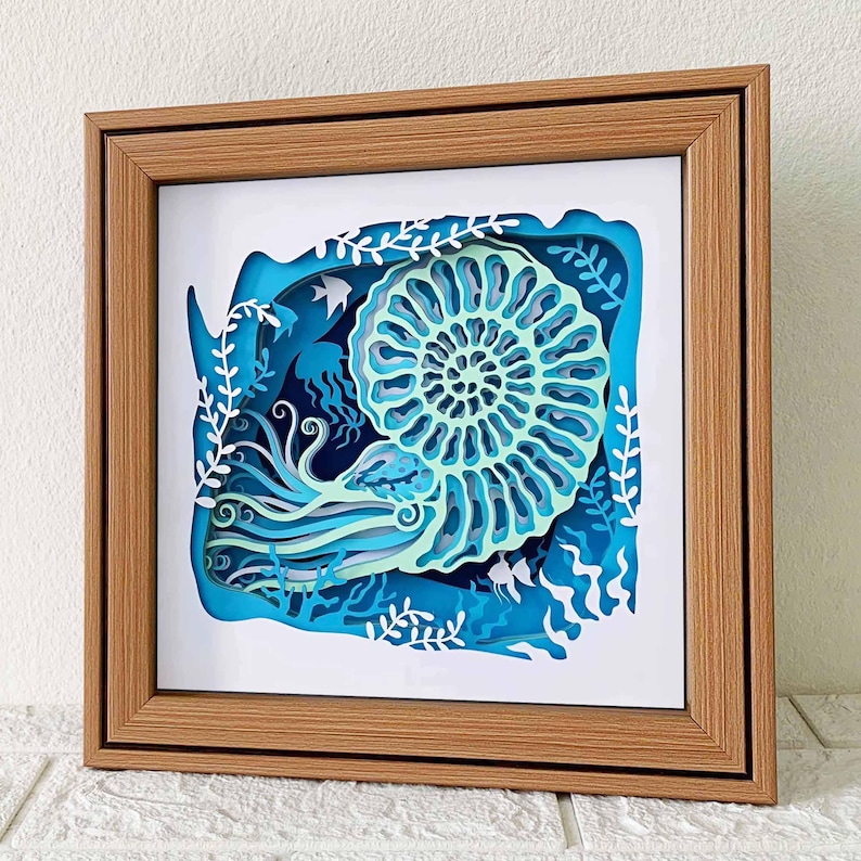 May include: A framed paper art piece depicting a nautilus shell with swirling patterns in shades of blue and green. The shell is surrounded by seaweed and fish, creating an underwater scene.