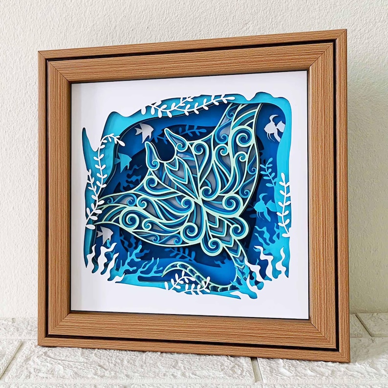 May include: A wooden frame with a white mat and a blue and white paper cut-out of a manta ray in a blue ocean scene.