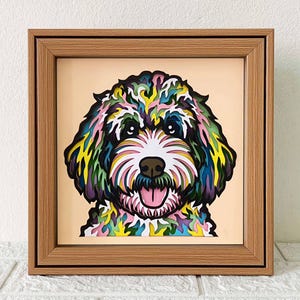 Könnte beinhalten: Ein farbenfroher, mehrschichtiger Papierschnitt eines Hundekopfes in einem Holzrahmen. Der Hund hat ein weißes Gesicht mit schwarzen Augen und einer rosa Zunge. Das Fell ist eine Mischung aus Grün, Blau, Gelb und Rosa.