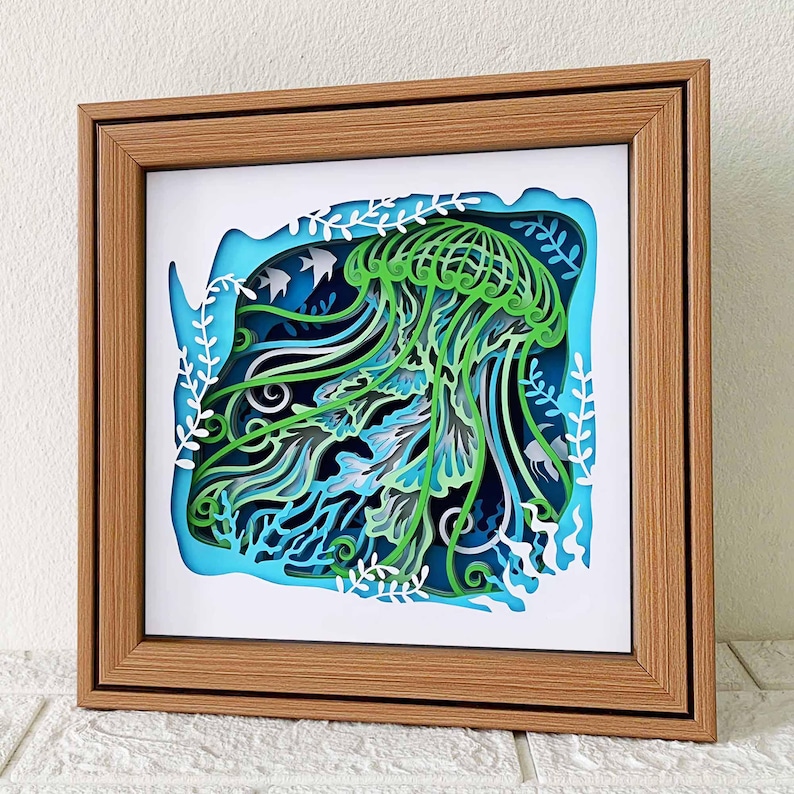 May include: A wooden frame with a 3D paper cut-out of a green jellyfish with blue and white accents. The jellyfish is surrounded by white paper cut-out seaweed and coral.