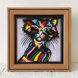 Può includere: Un'opera d'arte incorniciata raffigurante un gatto colorato. Il gatto è rappresentato con colori vivaci come rosso, giallo e blu. L'opera d'arte ha un design a strati. La cornice è in legno marrone chiaro.