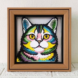 May include: A colorful paper cut-out of a cat's face in a wooden frame. The cat's fur is a rainbow of colors, including yellow, green, blue, and pink.