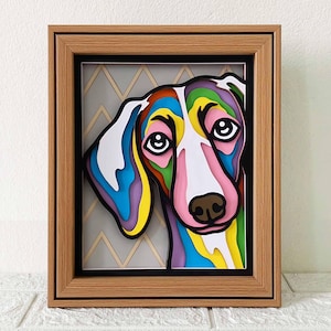 Könnte beinhalten: Ein farbenfrohes, mehrschichtiges Papierkunstwerk eines Hundekopfes in einem Holzrahmen. Das Fell des Hundes ist in Blautönen, Grün, Gelb und Rosa dargestellt. Der Hintergrund ist ein graues und goldenes Chevron-Muster.