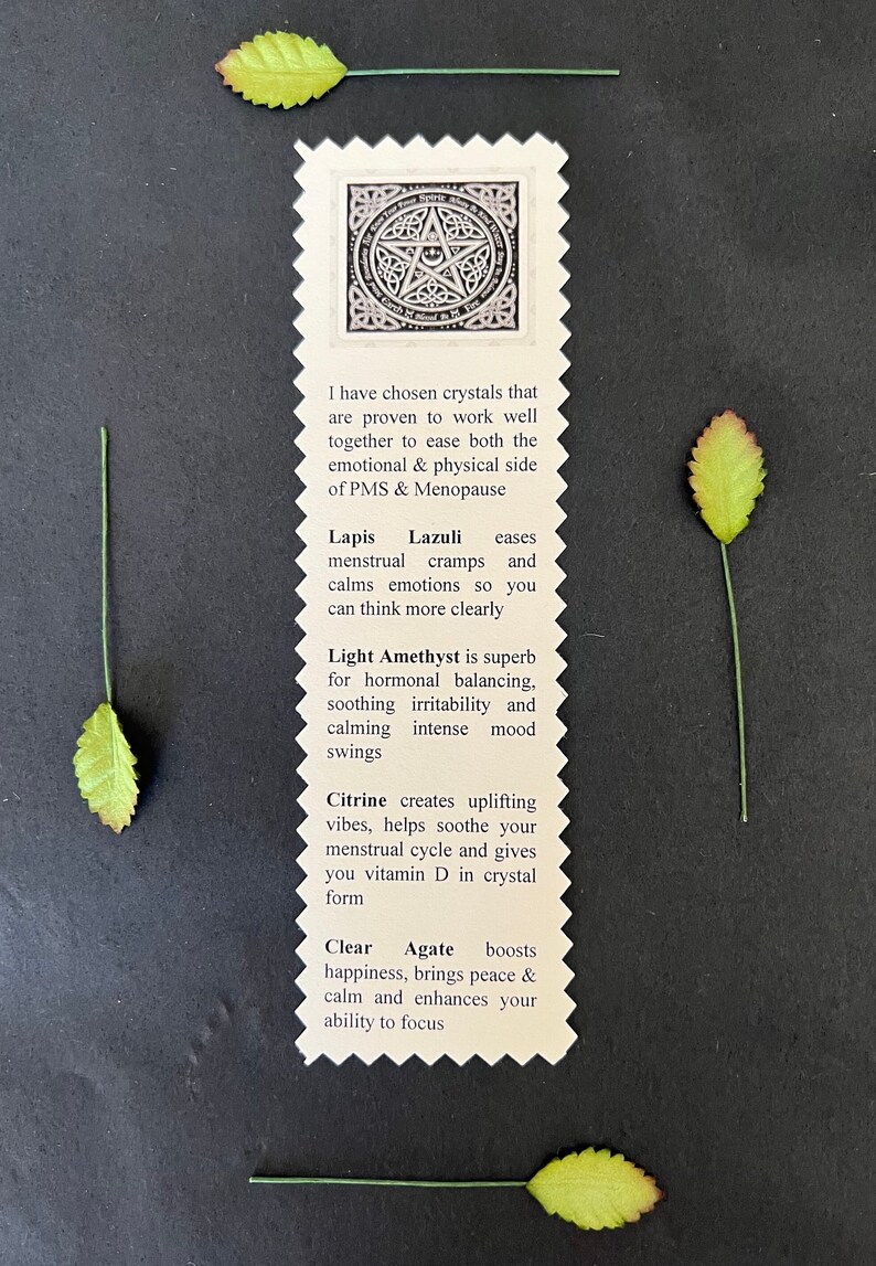 May include: A cream-colored card with a pentagram design and text about crystals for PMS and menopause, surrounded by four green leaves with red tips. The card lists crystals like Lapis Lazuli and Citrine.