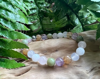 May include: A bracelet made of various coloured gemstone beads, including green, white, purple, and brown. The beads are strung on a silver metal chain.