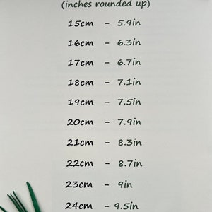 May include: A white paper with the text "Size Conversion" and a list of centimeter to inch conversions. Measurements range from 15cm (5.9in) to 24cm (9.5in). Green decorative leaves are in the corners.