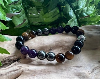 May include: A beaded bracelet featuring black, brown, purple, and silver beads. The bracelet is crafted from natural stones and is designed to be worn on the wrist.