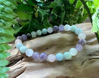 May include: A multi-coloured beaded bracelet with amethyst, rose quartz, and aquamarine beads. The bracelet is on a wooden surface.