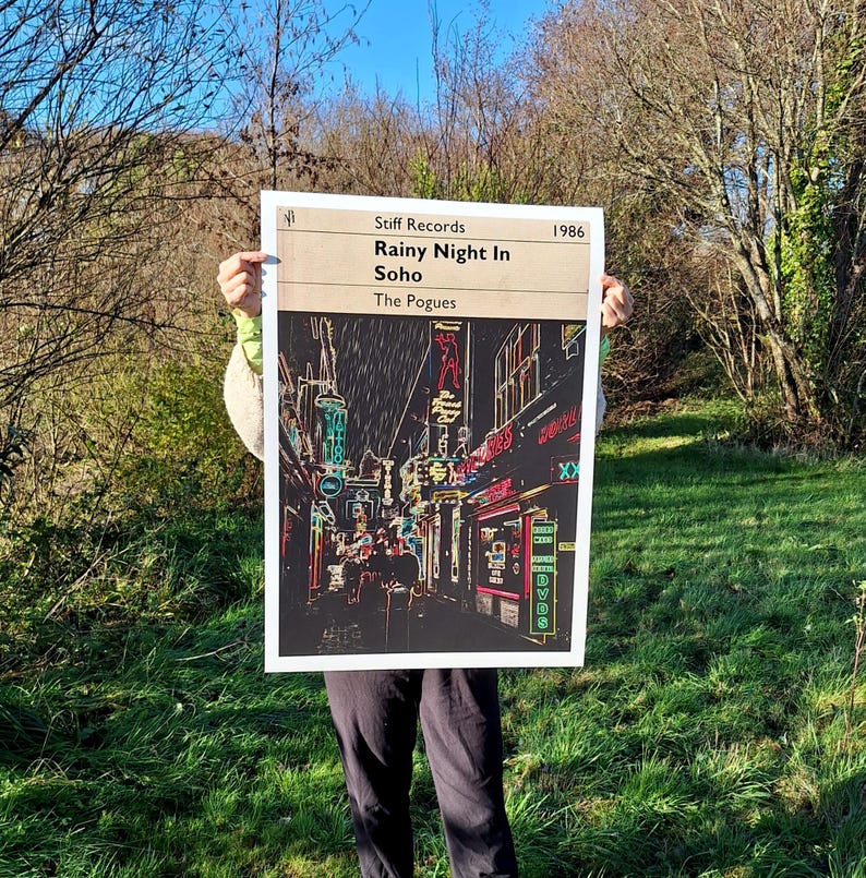 May include: A black and white poster with a neon-coloured image of a rainy street scene in Soho, London. The poster has the text "Stiff Records" and "Rainy Night In Soho" in white text. The text "The Pogues" is in white text below the title. The year "1986" is in white text in the upper right corner.