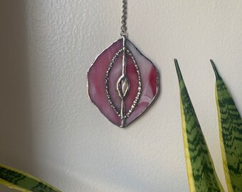 May include: A pink and white stained glass pendant with a silver chain. The pendant is shaped like a hexagon and has a swirling design.