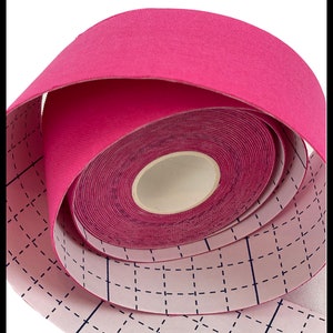 Puede incluir: Un rollo de cinta atl&eacute;tica rosa con un patr&oacute;n de cuadr&iacute;cula en el respaldo. La cinta est&aacute; enrollada y lista para usar.