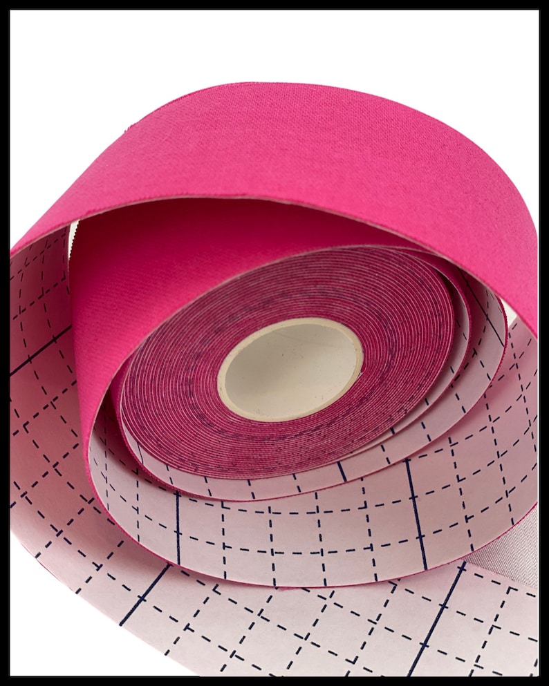 Puede incluir: Un rollo de cinta atl&eacute;tica rosa con un patr&oacute;n de cuadr&iacute;cula en el respaldo. La cinta est&aacute; enrollada y lista para usar.