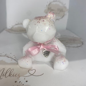 Op de afbeelding: Een wit geometrisch berenbeeldje met roze glitter en een roze lint. De beer heeft een zilveren hanger met de tekst "made with love".