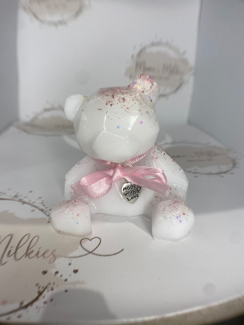 Op de afbeelding: Een wit geometrisch berenbeeldje met roze glitter en een roze lint. De beer heeft een zilveren hanger met de tekst "made with love".