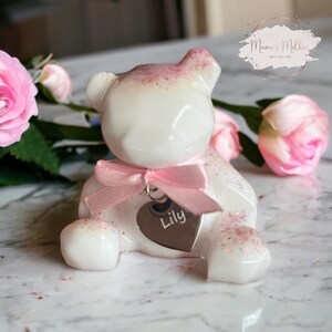 Op de afbeelding: Een witte teddybeer van hars met roze glitteraccenten en een roze lint om zijn nek. De beer heeft een zilveren hartbedel met de naam "Lily" erop gegraveerd.