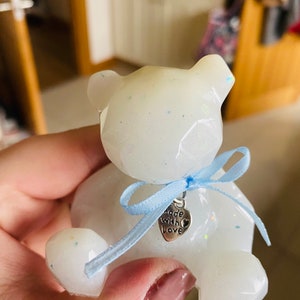 Op de afbeelding: Witte teddybeer van hars met glitter, met een blauw lint met een zilveren bedel waarop "Made with Love" staat.