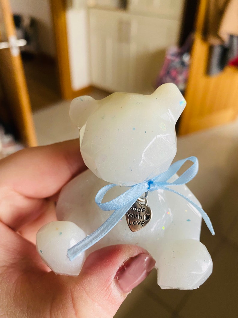 Op de afbeelding: Witte teddybeer van hars met glitter, met een blauw lint met een zilveren bedel waarop "Made with Love" staat.
