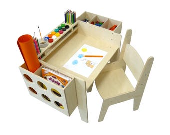Può includere: Un set di tavolo e sedia per bambini in legno con scomparti per riporre gli accessori per l'arte. Il tavolo ha un porta matite incorporato, un porta bicchieri per la vernice e un porta rotolo di carta. La sedia è in legno e ha un design semplice.