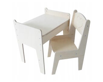 Può includere: Un set di tavolo e sedia in legno bianco per bambini. Il tavolo ha un piccolo cassetto e la sedia ha un'apertura a forma di cuore sullo schienale.