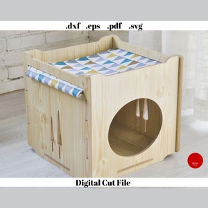 May include: A wooden cat house with a removable cushion top and a round entrance hole. The house is light brown and has a geometric pattern on the cushion. The text "Digital Cut File" is printed below the house.