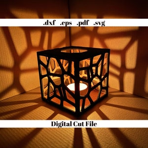 Puede incluir: Un portavelas geométrico negro con una vela de té dentro. El portavelas está hecho de madera y tiene un diseño de celosía. El portavelas proyecta sombras sobre la superficie en la que está sentado. El texto '.dxf .eps .pdf .svg' y 'Digital Cut File' son visibles en la imagen.