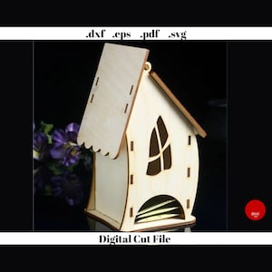 May include: A wooden tea bag holder shaped like a house with a window and a roof. The holder is made of light wood and has a slot for tea bags. The text "Digital Cut File" is printed below the holder.