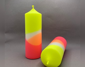 Könnte beinhalten: Zwei bunte Kerzen mit einem gelben, orangen und rosafarbenen Design. Die Kerzen sind zylindrisch und haben eine glatte Oberfläche.