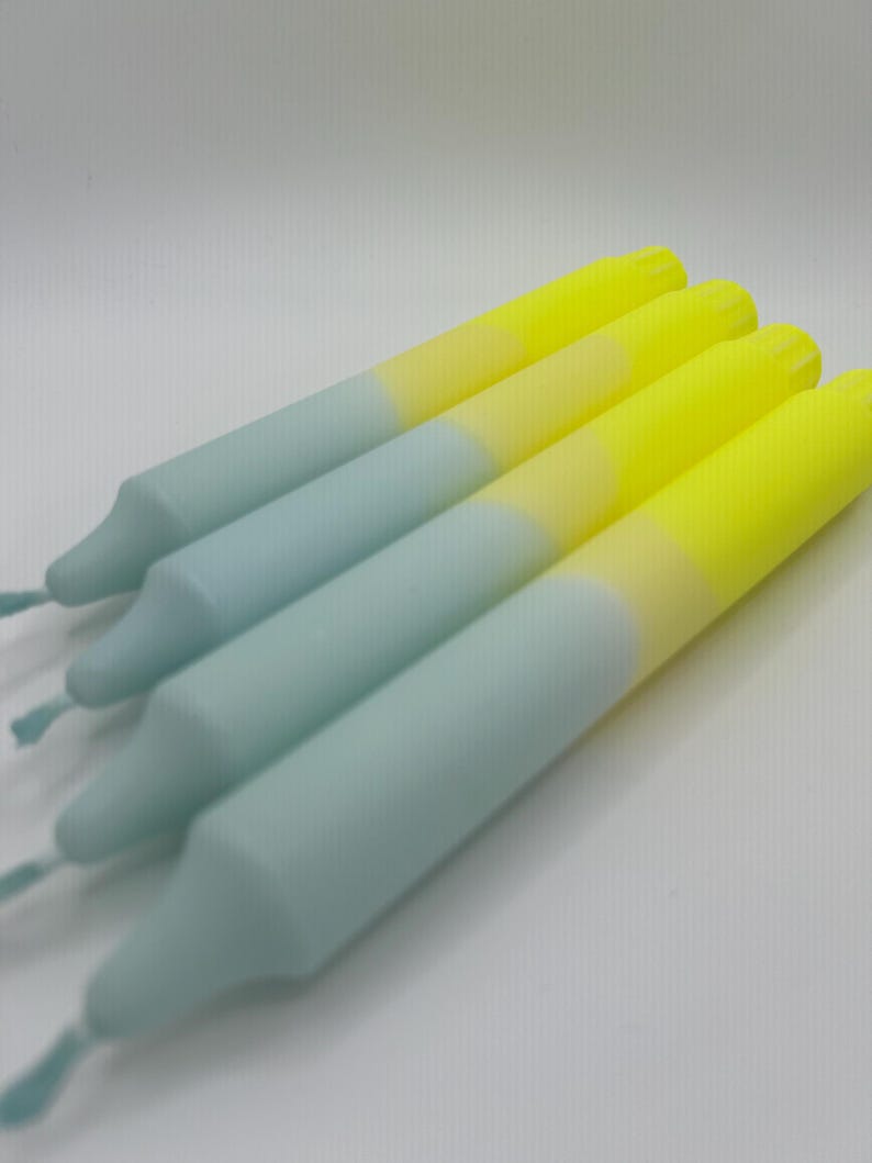 K&ouml;nnte beinhalten: Vier Ombre-Spitzenkerzen mit einem hellblauen und gelben Farbverlauf. Die Kerzen sind in einem Stapel angeordnet, wobei die gelben Enden nach oben zeigen.