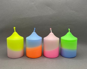 Könnte beinhalten: Vier farbige Säulenkerzen mit Farbverlauf. Jede Kerze hat eine andere Farbkombination: Gelb und Rosa, Blau und Orange, Rosa und Magenta sowie Grün und Blau. Die Kerzen sind zylindrisch mit einer kleinen, spitzen Spitze.