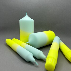 K&ouml;nnte beinhalten: Ein Set aus f&uuml;nf Kerzen in einem hellblauen und gelben Ombre-Design. Die Kerzen sind in einer Gruppe auf einer grauen Oberfl&auml;che angeordnet.
