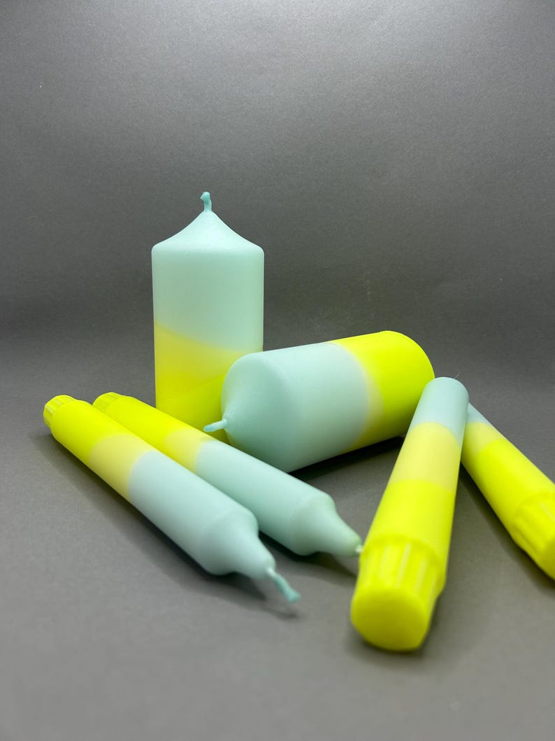 K&ouml;nnte beinhalten: Ein Set aus f&uuml;nf Kerzen in einem hellblauen und gelben Ombre-Design. Die Kerzen sind in einer Gruppe auf einer grauen Oberfl&auml;che angeordnet.