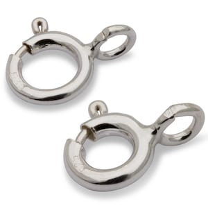 Könnte beinhalten: Zwei silberfarbene Federringverschlüsse. Diese Schmuckteile haben ein kreisförmiges Design mit einem kleinen Hebel zum Öffnen und Schließen. Die Verschlüsse befinden sich auf weißem Hintergrund.