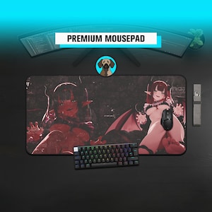 May include: A large rectangular mousepad with a dark background featuring two anime-style female figures. The mousepad has the text "PREMIUM MOUSEPAD" and a small keyboard and mouse are visible.