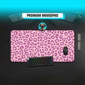 May include: A rectangular mousepad featuring a pink and magenta leopard print pattern. The mousepad is positioned on a dark surface with a black mechanical keyboard and a black computer mouse placed on top of the surface of the mousepad.