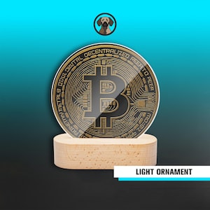 Puede incluir: Adorno luminoso Bitcoin redondo, negro y dorado. El símbolo de Bitcoin está centrado en el adorno, con las palabras "Descentralizado" y "Digital" alrededor del borde. El adorno se asienta sobre una pequeña base de madera redonda. El texto "LIGHT ORNAMENT" se muestra debajo.